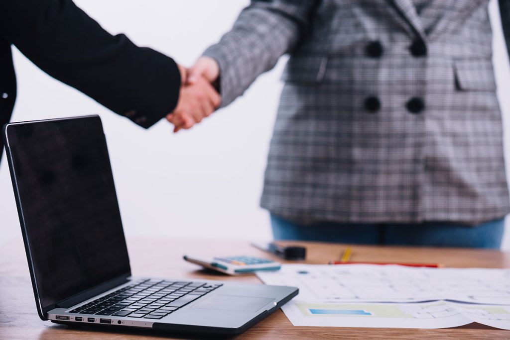 Laptop near people shaking hands